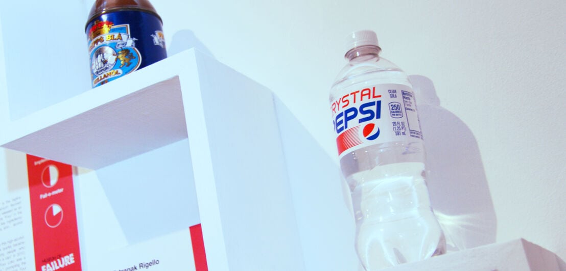 Eine Plastikflasche der Marke Crystal Pepsi mit durchsichtiger Flüssigkeit als Ausstellungsstück an einer Wand