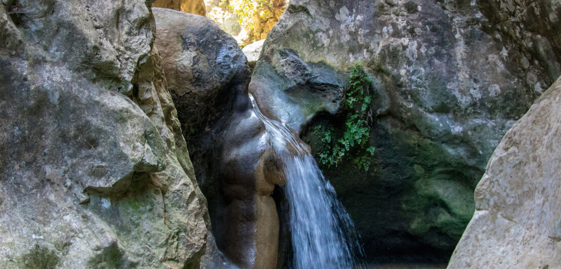 Ein Wasserfall fällt zwischen zwei Felswänden in ein natürliches Wasserbassin
