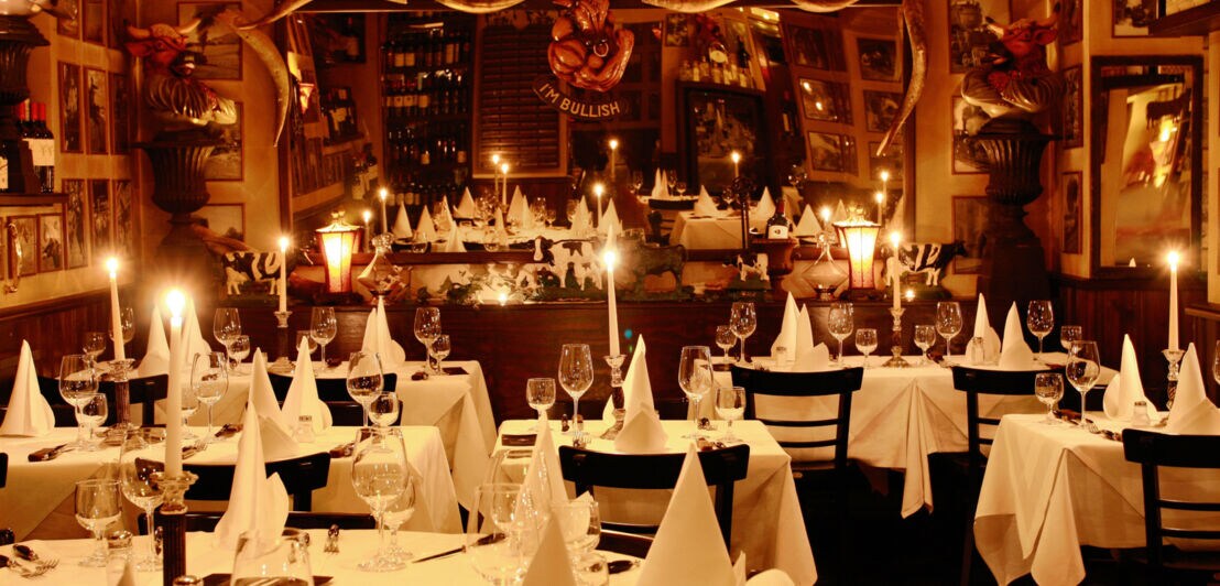 Tische mit weißen Decken, gefalteten Servietten und brennenden Kerzen im M-Steakhouse