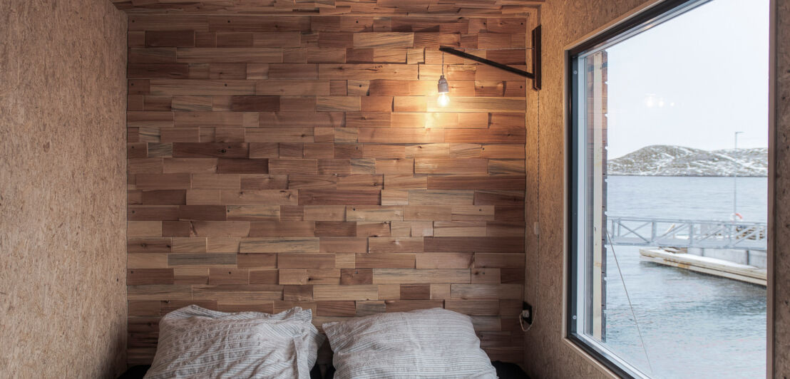 Ein mit Holz verkleideter Raum mit Schlafnische und großem Fenster, das eine Sicht aufs Meer bietet