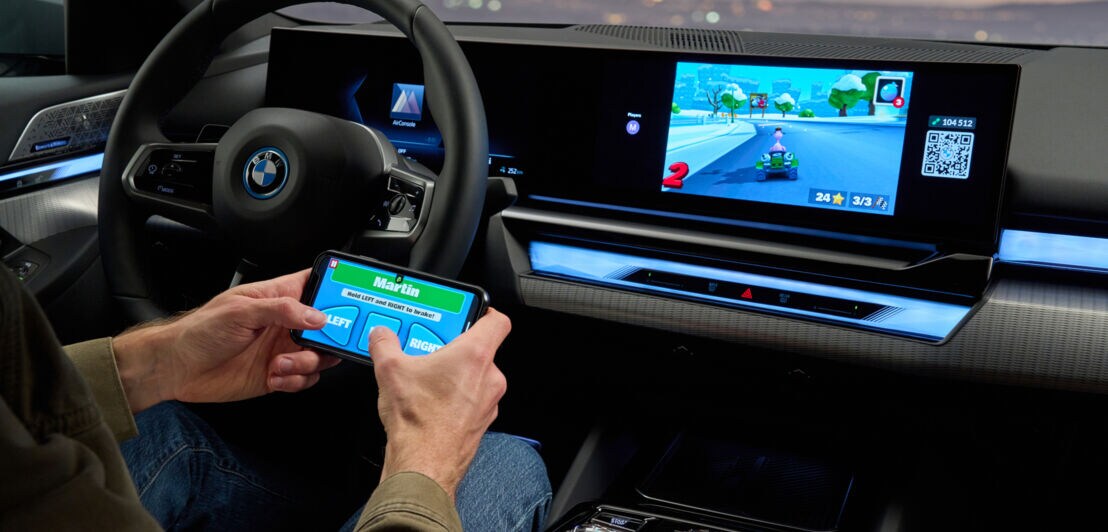 Eine Person sitzt im Auto und bedient über ihr Smartphone die AirConsole im BMW i5.