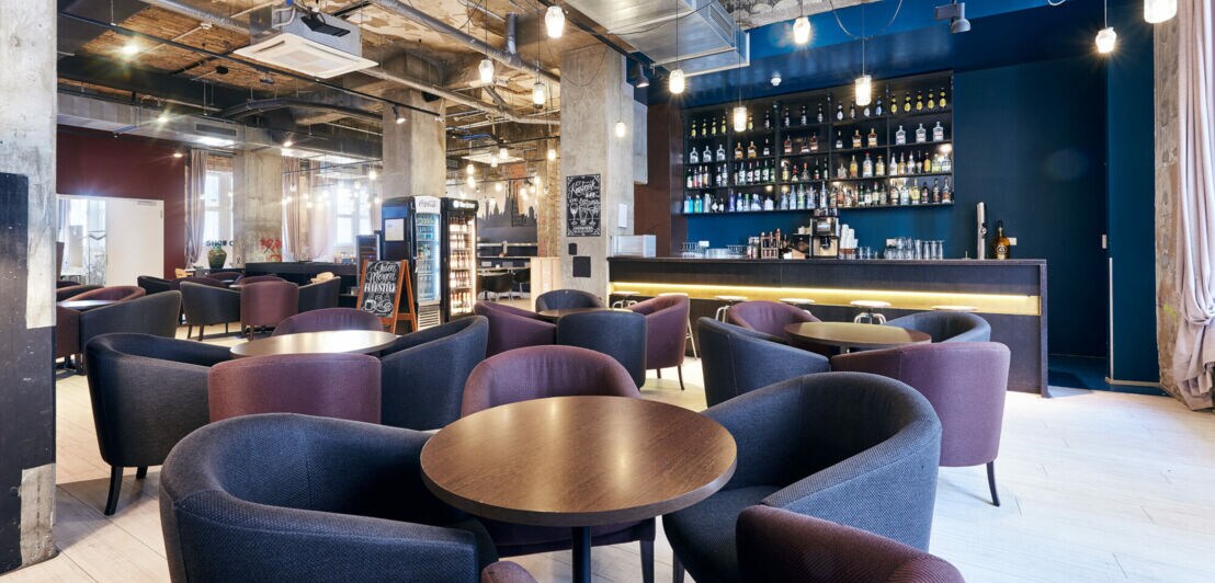 Eine Hotellobby mit Sitzgelegenheiten vor einer Bar unter einer offenen Raumdecke im Industriestil.