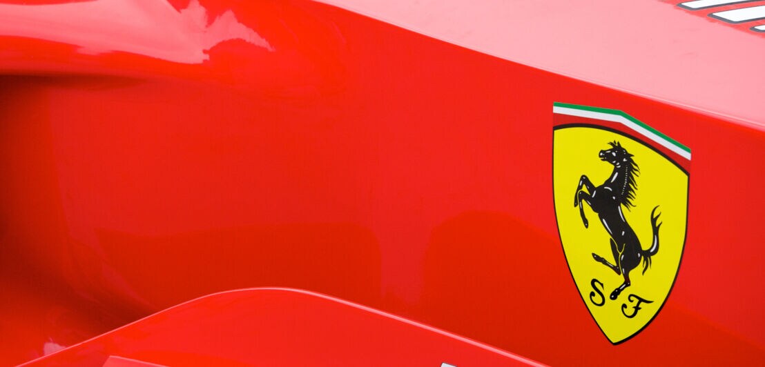 Detailaufnahme eines roten Rennwagens des Herstellers Ferrari mit dem Markenlogo eines sich aufbäumenden Pferdes in einem gelben Wappen