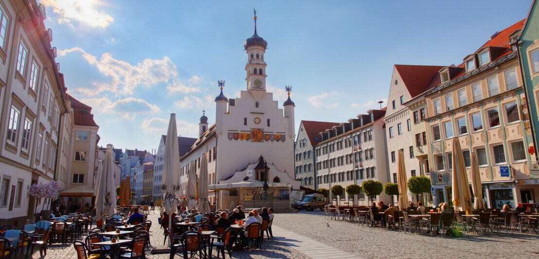 Altstadt von Kempten mit Personen, die in Cafés auf dem Marktplatz vor einer Kirche sitzen