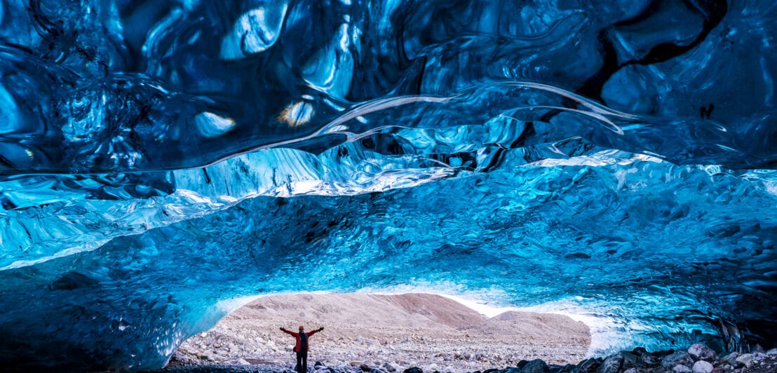 Eine Person steht am Eingang einer Eishöhle 