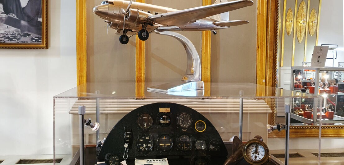 Glasvitrine mit antiken Bordinstrumenten, auf der sich ein metallisch glänzendes Flugzeugmodell befindet
