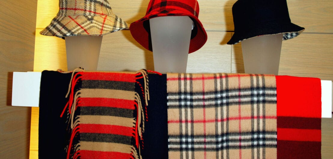 Hüte und Schals mit Karos und Streifen in einem Schaufenster.