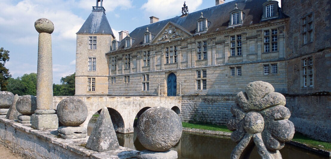 Ein französisches Wasserschloss mit Brücke und Steinskulpturen auf einer Mauer im Vordergrund