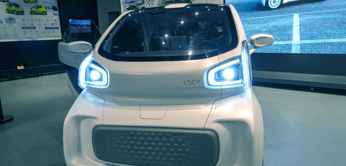 Das Elektrokleinfahrzeug XEV Yoyo steht in einer Ausstellungshalle neben einer Leinwand