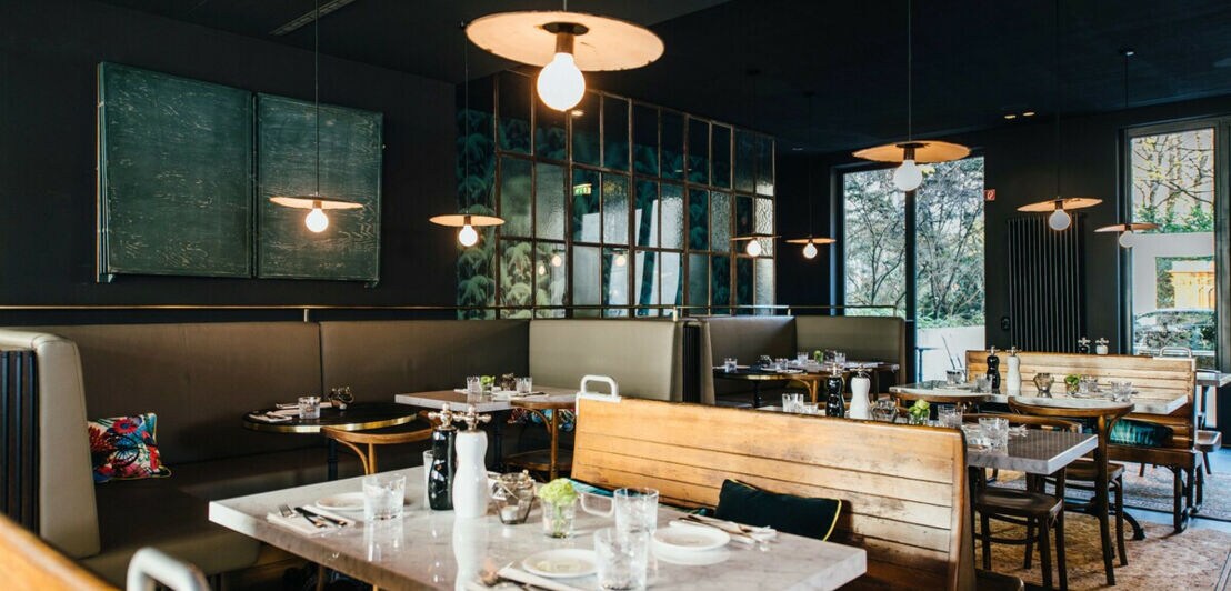 Holzbänke und gedeckte Tische in der Brasserie Colette in München