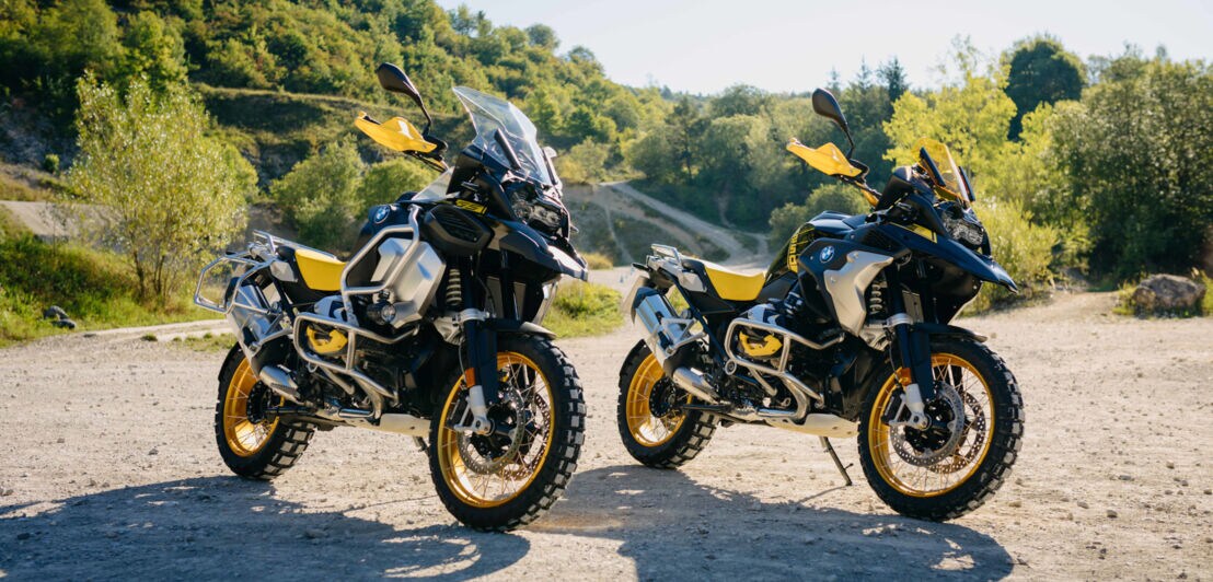 Zwei sportliche BMW-Motorräder R 1250 GS im schwarz-gelben Design stehen nebeneinander an einer Waldlichtung
