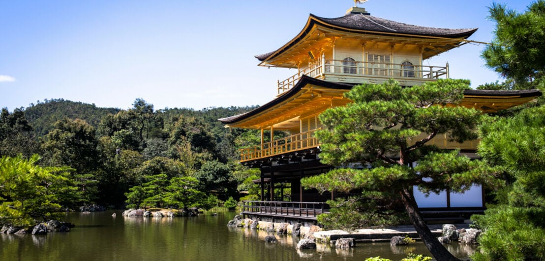 Mehrstöckige, goldene buddhistische Tempelanlage an einem See in einem japanischen Garten