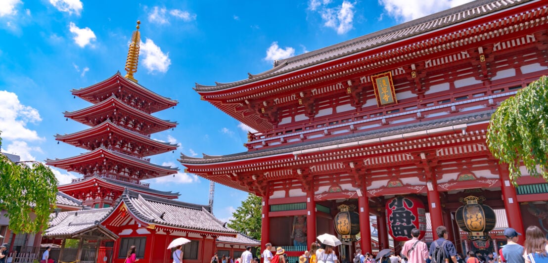 Besucher:innen stehen vor einem roten Tempelgebäude und einer roten Pagode