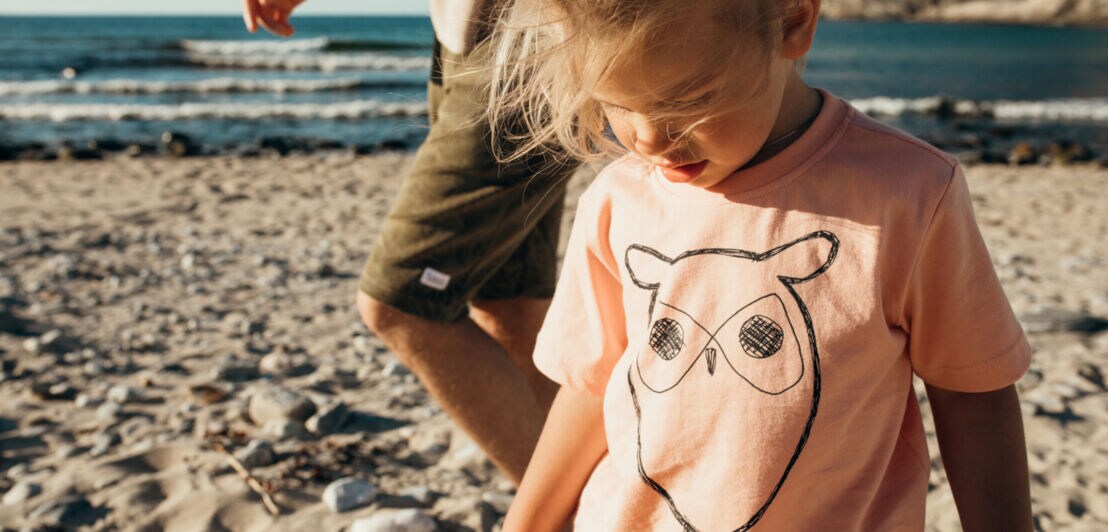 Ein kleines Mädchen am Strand trägt ein T-Shirt mit Eulen-Print