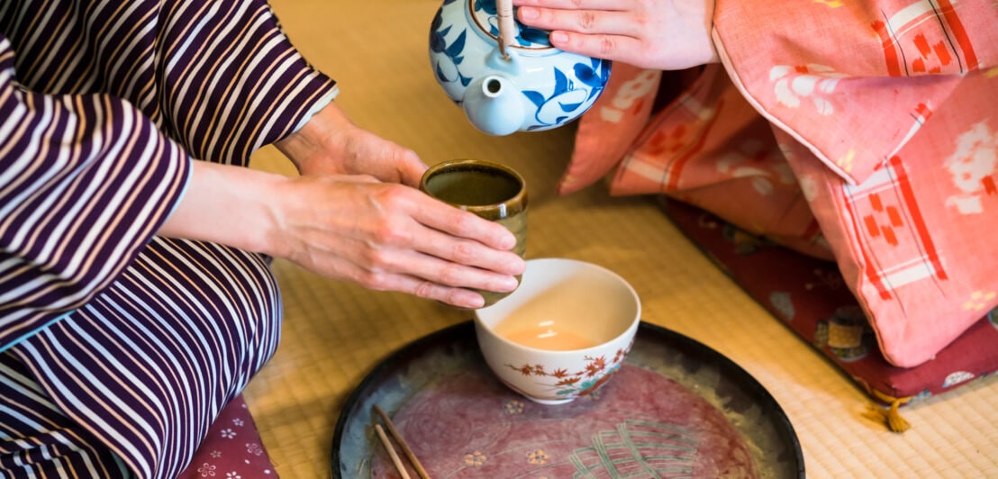 Detailaufnahme einer traditionellen japanischen Teezeremonie mit zwei Frauen in gemusterten Kimonos