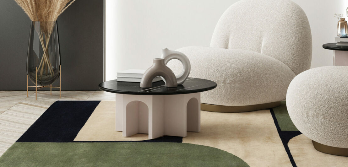 Auf einem Teppich mit geometrischem Muster stehen ein runder Tisch und zwei Sessel