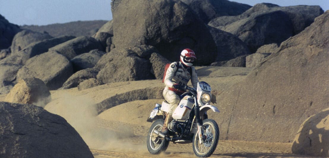 Ein Motorradfahrer auf einer weißen BMW R 80 G/S fährt durch eine Wüstenlandschaft, verblasste Fotoaufnahme