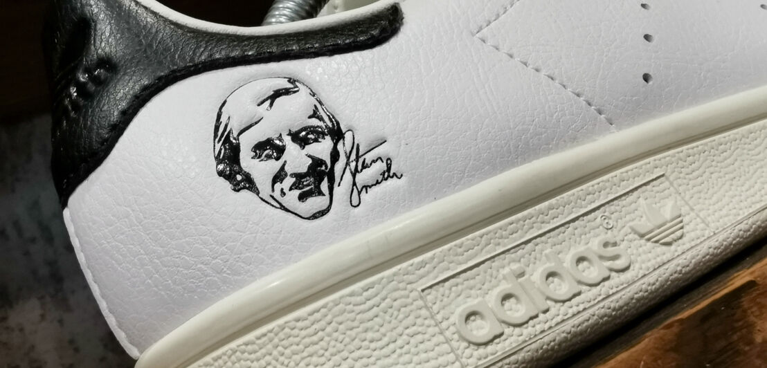 Weiß-schwarzer Adidas-Schuh mit aufgedrucktem Kopf und Schriftzeichen von Stan Smith