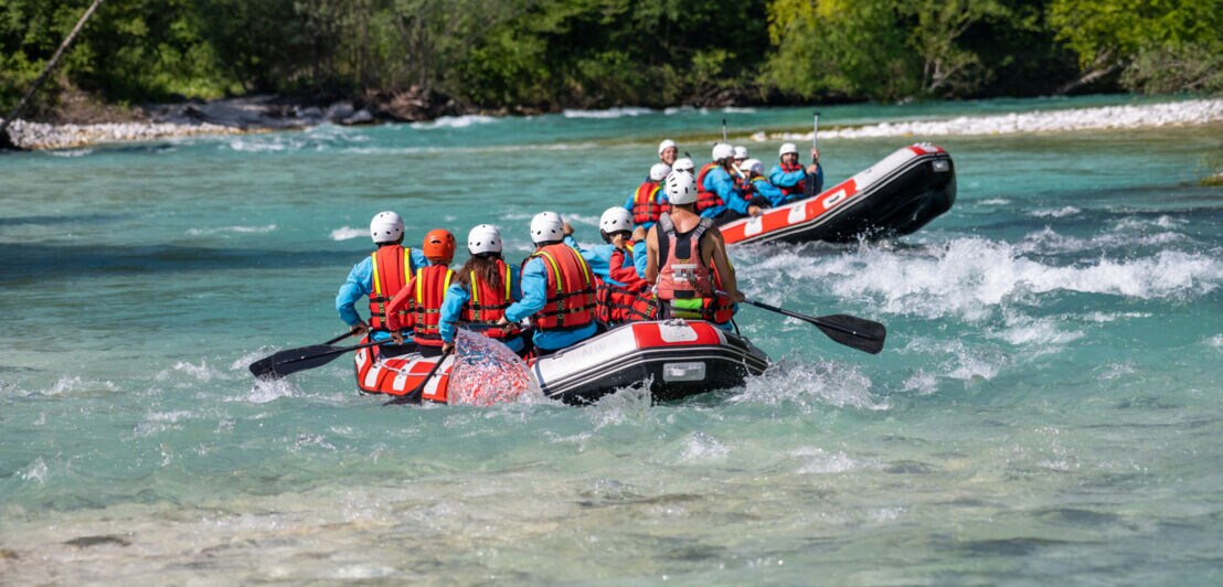 Zwei Gummiboote mit mehreren Personen paddeln einen Fluss hinab