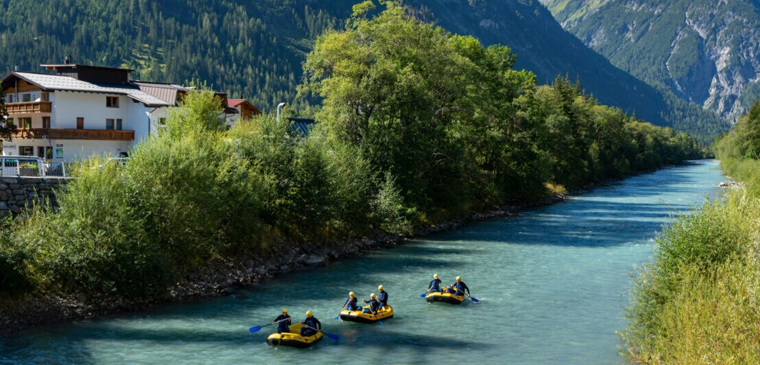 Mehrere Personen fahren in drei gelben Schlauchbooten auf einem Fluss durch eine Berglandschaft