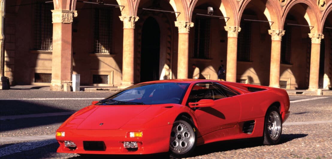 Ein roter Lamborghini Diablo VT parkt vor einem Gebäude mit Rundbögen