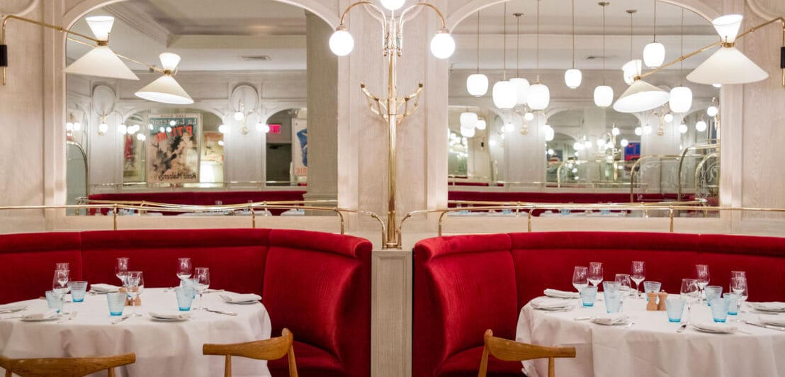 Interieuraufnahme eines edlen Restaurants mit gedeckten, runden Tischen und Sitzbänken aus rotem Samt.