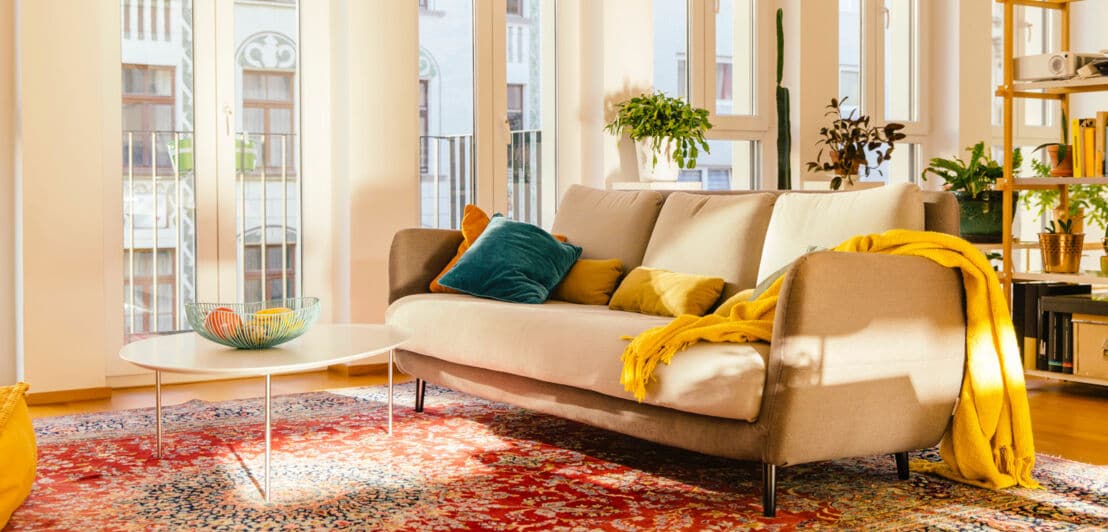 Roter Perserteppich in einer modern eingerichteten Wohnung mit beigefarbener Couch und vor großer Fensterfront