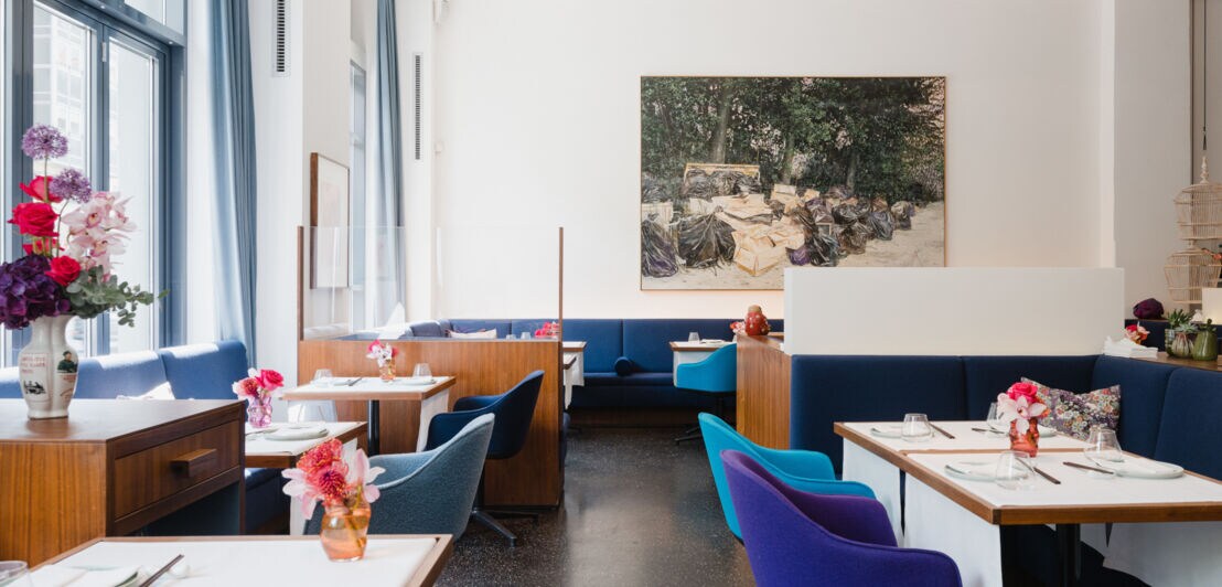 Interieuraufnahme eines modernen, minimalistisch eingerichteten Restaurants mit gedeckten Tischen und Polstermöbeln aus blauem Samt.
