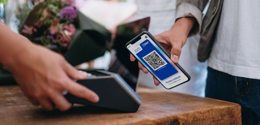 Eine Person bezahlt kontaktlos via Mobile Pay in einem Blumenladen mit einem QR-Code in der PAYBACK-App