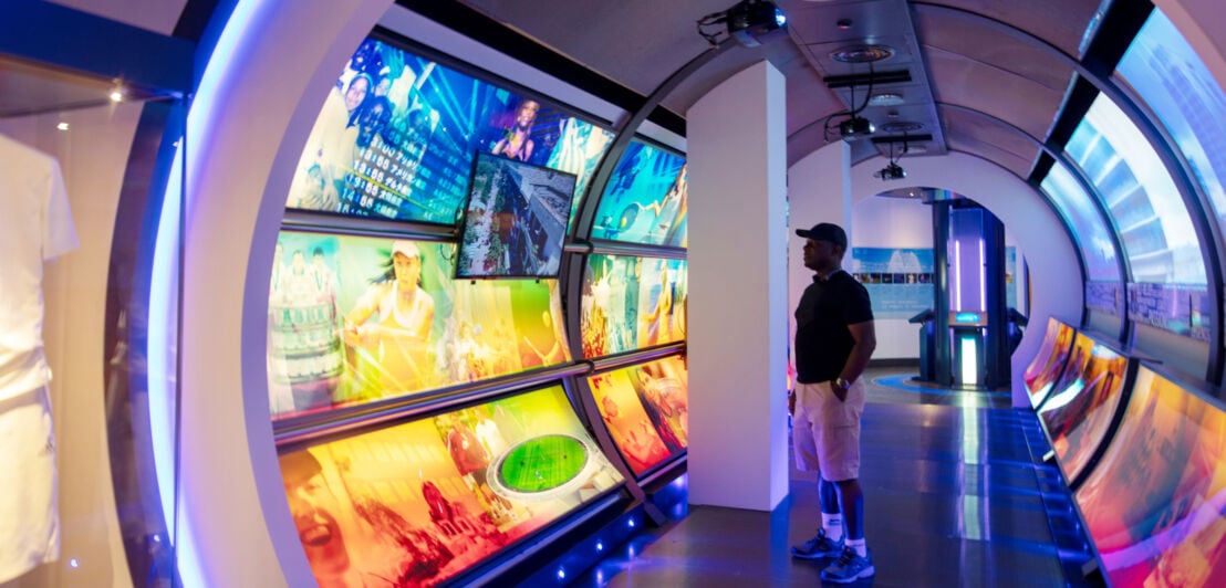 Ein Besucher in einem futuristischen Ausstellungsraum in einem Rundbogen mit digitalen Bildern zum Thema Tennis