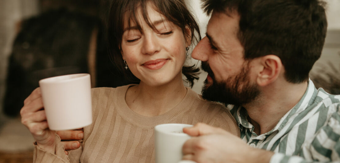 Nahaufnahme eines glücklichen, aneinander gekuschelten Paares mit Kaffeetassen