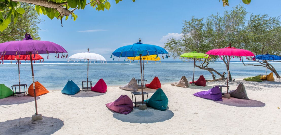 Bunte Sonnenschirme und Sitzsäcke an einem Strand auf den Gili Islands nahe Bali