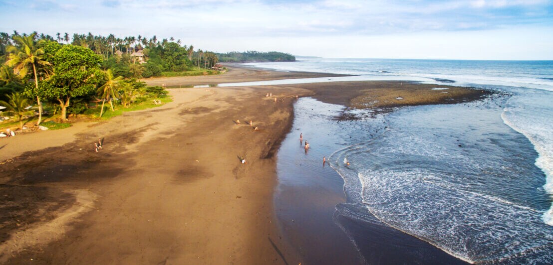 Weitläufiger, naturbelassener Strand mit dunklem Sand und vereinzelten Badegästen