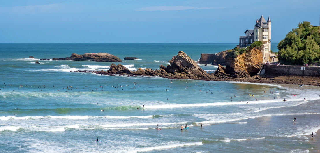 Zahlreiche Personen mit Surfbrettern im Wasser vor der Küste von Biarritz