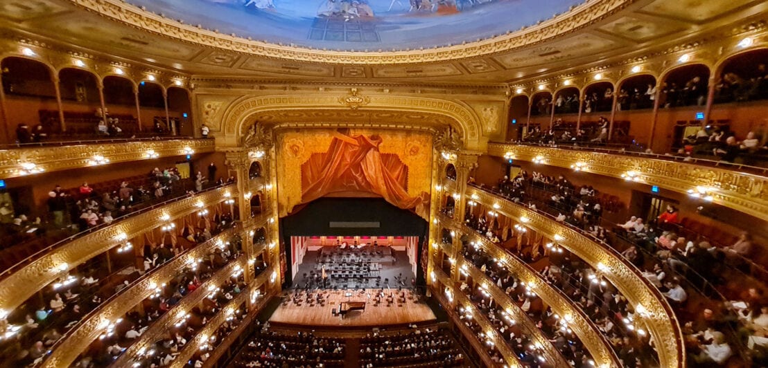 Klavierkonzert mit Publikum in einem prachtvollen, runden Opernsaal mit Goldverzierungen, roten Sesseln und blauem Deckenfresko