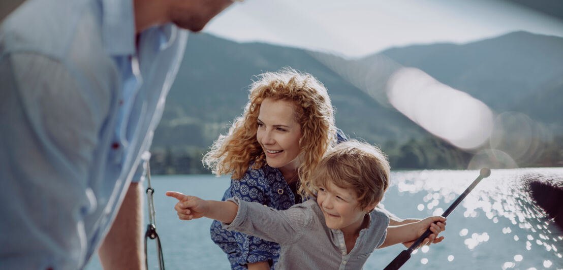 Ein kleiner Junge mit seinen Eltern auf einem Segelboot auf dem Meer zeigt mit dem Finger in die Ferne