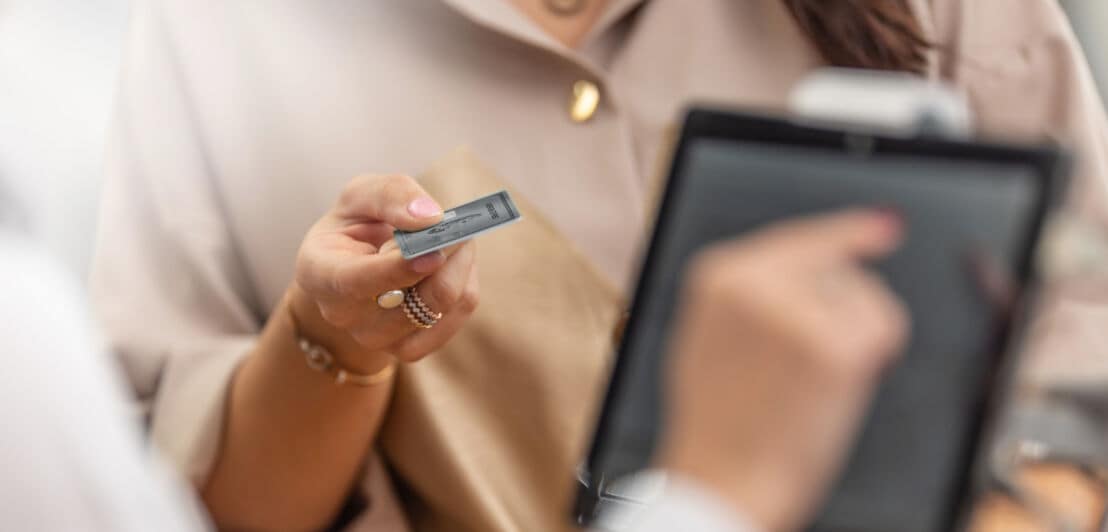 Nahaufnahme einer Kundin, die an der Kasse eines Geschäfts mit einer silbernen Kreditkarte aus Metall in ihrer Hand bezahlt