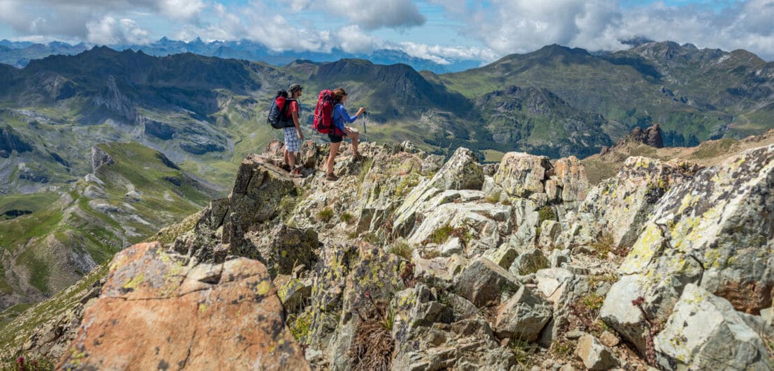 Zwei Wandernde mit Rucksäcken auf einem Gipfel vor Bergpanorama