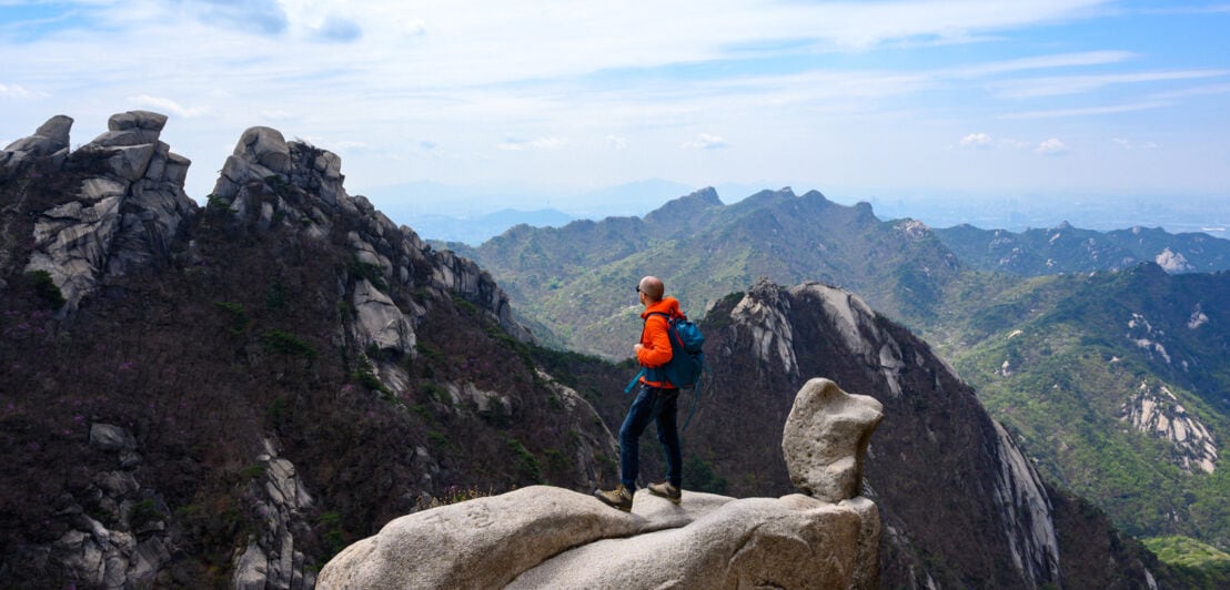 Ein Wanderer steht auf einem Felsgipfel und blickt über die Landschaft im Bukhansan Nationalpark