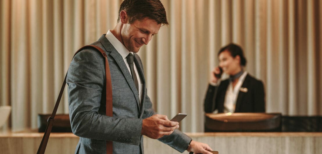 Ein Geschäftsmann schaut lächelnd auf sein Smartphone in einer Hotellobby