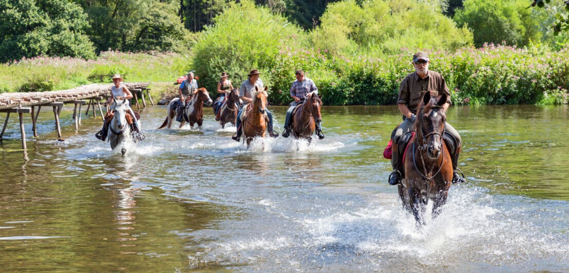 Eine Personengruppe durchquert auf Pferden einen Fluss