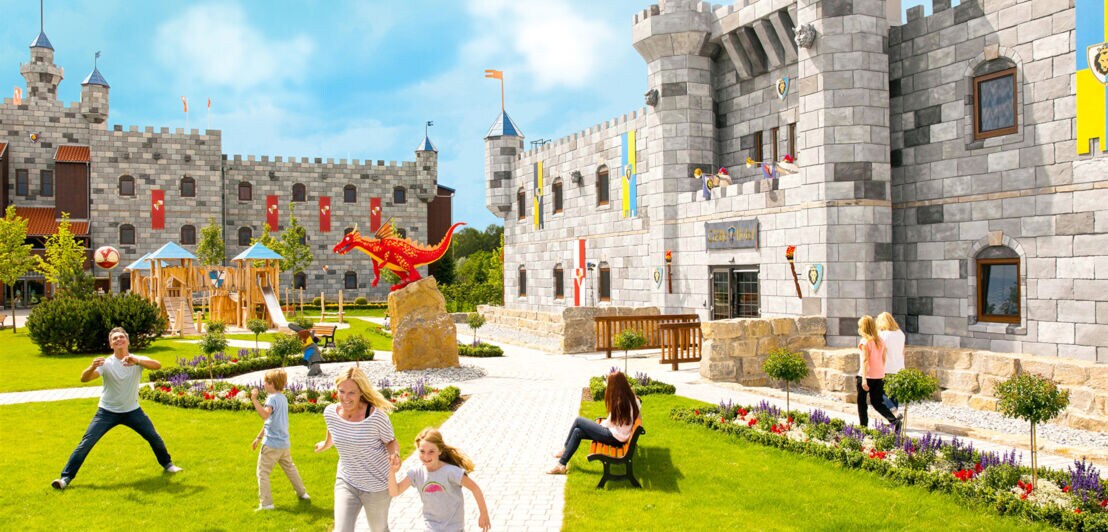 Mehrere Kinder und Erwachsene in einem Park vor einem künstlichen Schloss in einem Freizeitpark