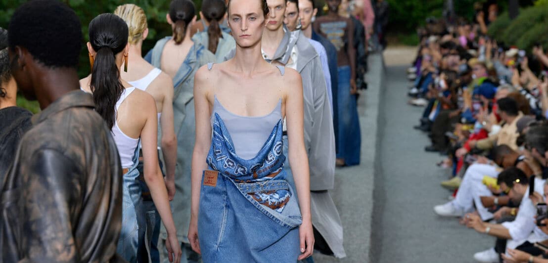 Models in avantgardistischer Jeanskleidung laufen in Reihe auf einem Laufsteg bei einer Modenschau im Freien