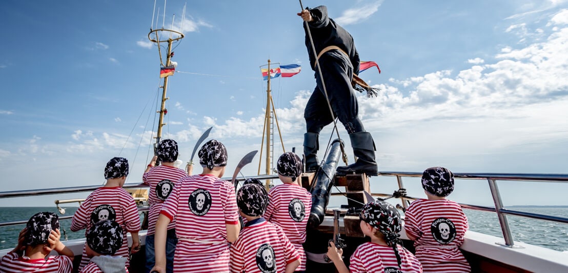 Ein verkleideter Pirat mit Kindern am Bug eines Schiffes auf dem Meer