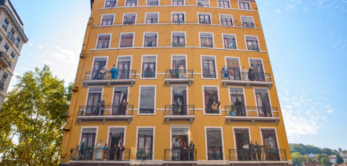 Ein Fresko an einer Hauswand, das unterschiedliche Personen auf Balkonen darstellt