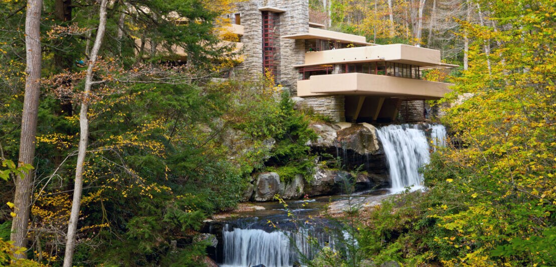Eine mehrstöckige, über einen Wasserfall gebaute Villa in einem Waldgebiet