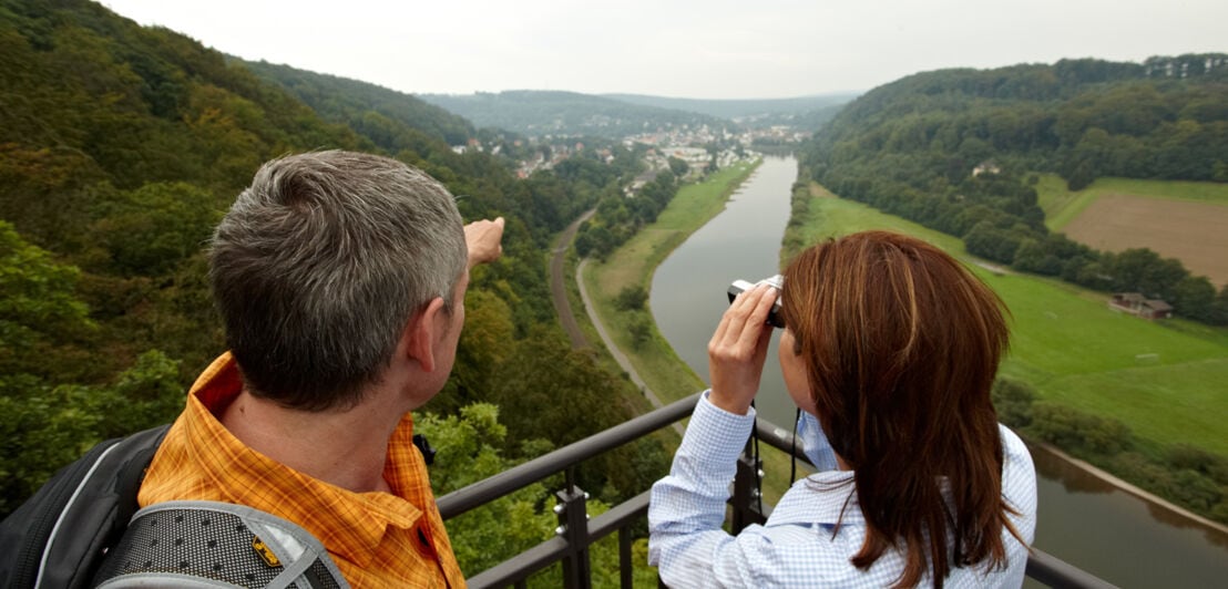Zwei Personen stehen auf einer Erhöhung und blicken mit einem Fernglas über die Weser hinweg