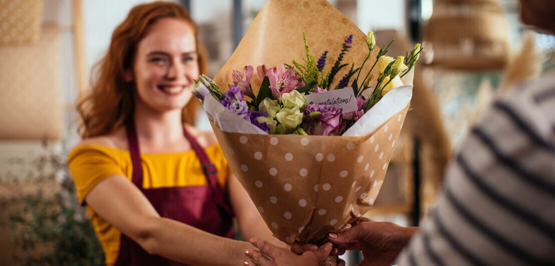 Eine junge Verkäuferin überreicht einem Kunden einen Blumenstrauß in einem Geschäft.