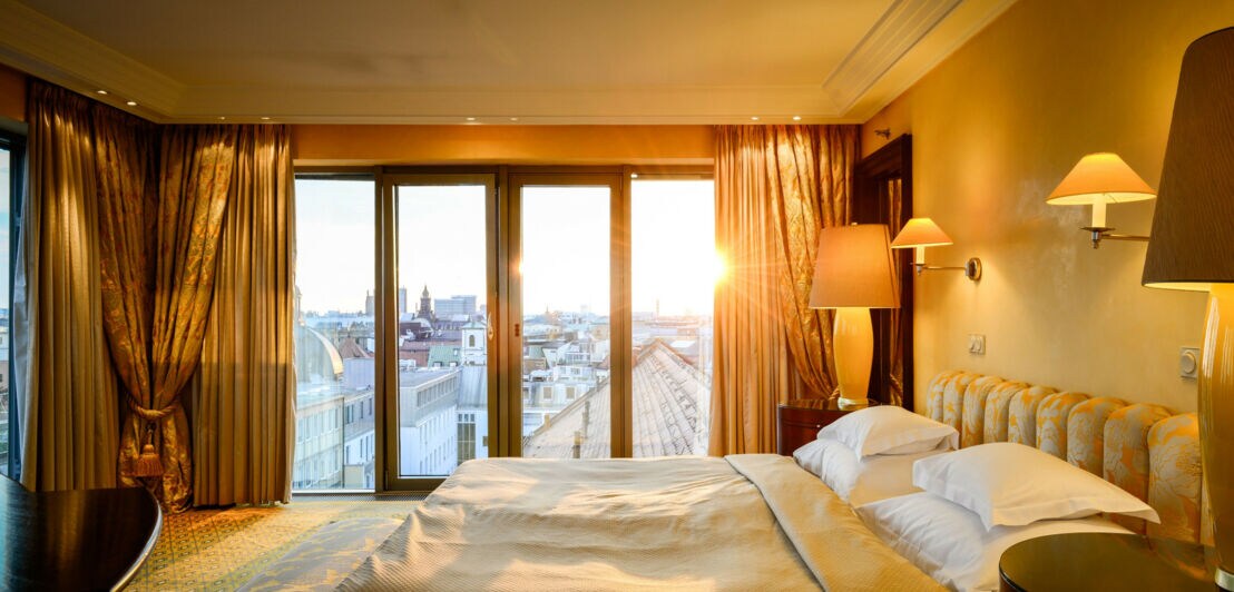 Elegante Hotelsuite mit goldenen Textilien und bodentiefen Fenstern mit Blick auf die Münchner Innenstadt