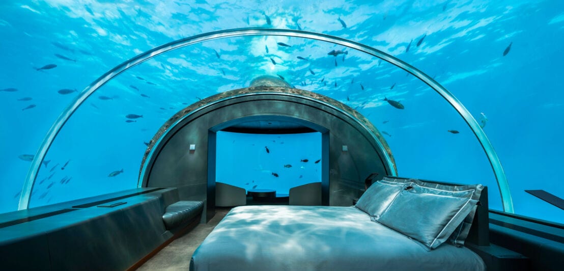Eine Unterwasserhotelsuite mit Glaskuppel, an der Fische vorbeischwimmen.
